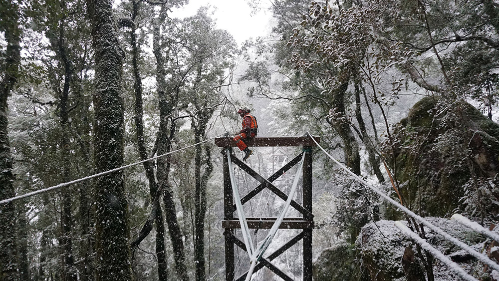 Abseil Access workers sitting on bridge poles in snowy weather.